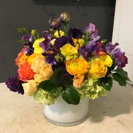 Colorful bouquet of roses and purple blooms in a white vase