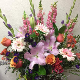 Mixed bouquet with pink lilies, roses, and tall snapdragons in a basket