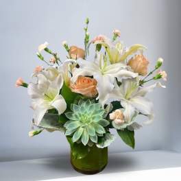 White lilies and peach roses in a green glass vase with a succulent accent