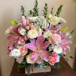Pink lilies and roses arranged in a square wooden box