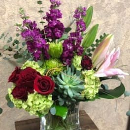 Bouquet of red roses, purple flowers, and lilies in a glass vase