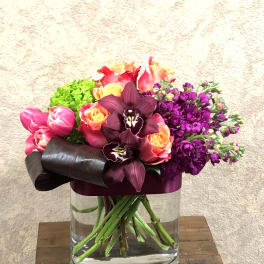 Mixed bouquet of pink, orange, purple, and green flowers in a glass vase