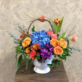 Colorful flower arrangement in a white pedestal vase with a twig handle