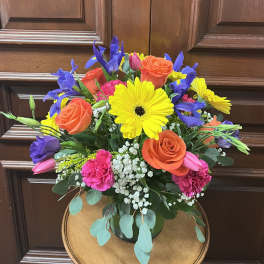 Bright mixed bouquet with yellow gerbera daisies, orange roses, and purple irises in a vase