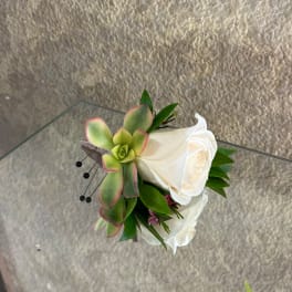 Small corsage with white roses and a green succulent on a glass surface