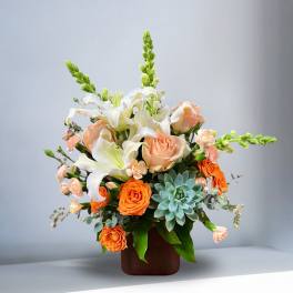 Peach roses and white lilies in a brown vase with a succulent accent