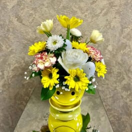 Yellow and white flower arrangement in a smiley-face vase