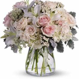 Arrangement of pale pink roses, white lilies, and hydrangeas in a clear glass vase