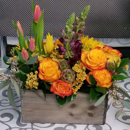 Mixed bouquet of orange roses, pink tulips, and purple blooms in a wooden box