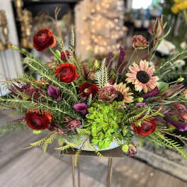Low floral arrangement with red ranunculus, sunflowers, and purple calla lilies