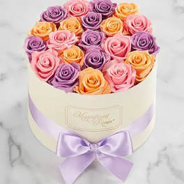 Round box of pink, purple, and peach roses with a lavender ribbon bow