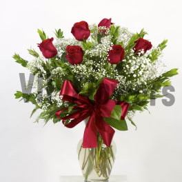 Red roses in a clear glass vase with baby's breath and a red ribbon
