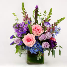 Mixed bouquet of pink, purple, and blue flowers in a glass vase