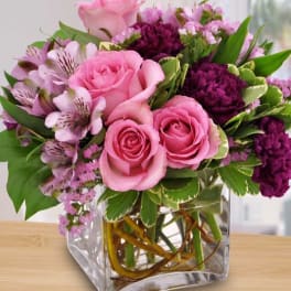 Pink roses and purple flowers arranged in a clear glass vase