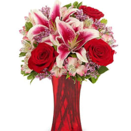 Red roses and pink lilies arranged in a red glass vase