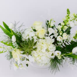 White floral arrangement with tulips, roses, and orchids in a low container