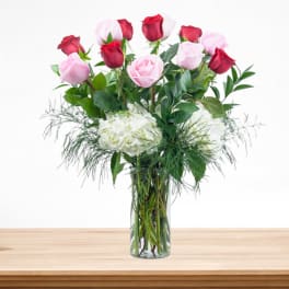 Pink and red roses in a clear glass vase with white hydrangeas
