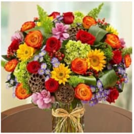 Mixed bouquet of roses, sunflowers, and small purple flowers in a glass vase