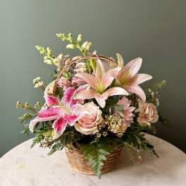 Pink lilies, roses, and mixed blooms arranged in a small wicker basket