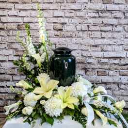 White floral arrangement with a dark urn centerpiece and ribbon accents