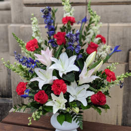 Tall red, white, and blue arrangement with lilies, roses, and carnations in a white pedestal vase