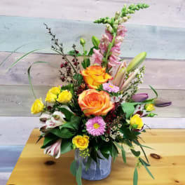 Mixed bouquet in a gray vase with orange roses, yellow spray roses, and pink blooms