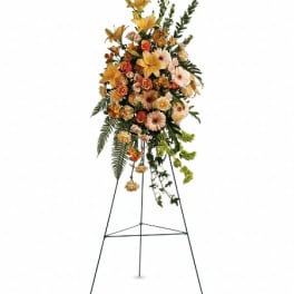 Tall standing spray with yellow lilies, peach roses, and gerbera daisies on a metal easel