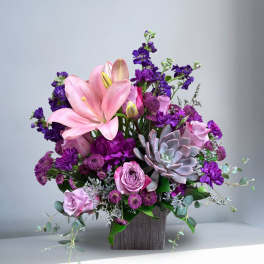 Pink lilies and roses with purple flowers in a wooden vase