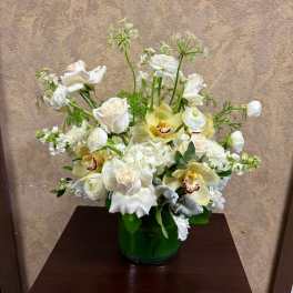 White floral arrangement with orchids and roses in a green vase