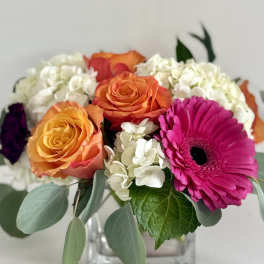 Bouquet of orange roses, white hydrangeas, and a pink gerbera daisy in a glass vase