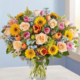 Mixed bouquet of roses, tulips, and sunflowers in a clear glass vase
