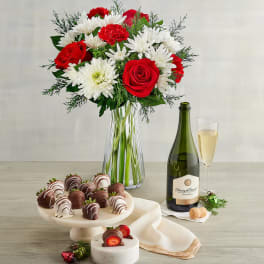 Bouquet of red roses and white daisies in a glass vase with champagne and chocolates