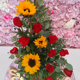 Red roses and sunflowers arranged in a tall vase with greenery