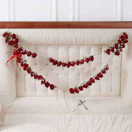 Red rose garlands draped across a white tufted headboard with a small cross