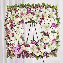 Floral standing wreath with white lilies, daisies, and pink blooms on an easel