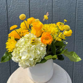 Yellow and white floral arrangement in a white vase with bee picks