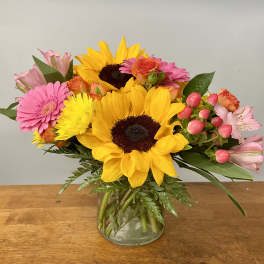 Mixed bouquet with sunflowers, pink gerberas, and roses in a glass vase