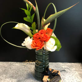 Orange and white roses in a tall glass vase with tropical leaves