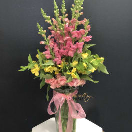 Pink and yellow flowers in a clear glass vase with a pink ribbon