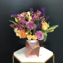 Mixed bouquet of roses and purple flowers in a pink geometric vase