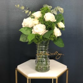 White roses arranged in a clear glass vase with green filler.