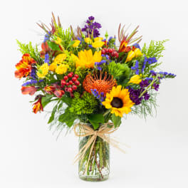 Bright mixed bouquet in a clear glass vase with a raffia bow