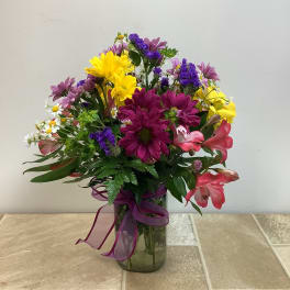 Mixed bouquet of daisies and lilies in a glass vase with a purple ribbon