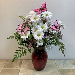 White daisy bouquet in a red glass vase with pink butterfly decorations