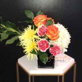 Bouquet of orange roses, yellow spider mums, pink carnations, and white hydrangea in a black vase
