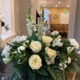 White floral arrangement with roses and lilies around a glass cross