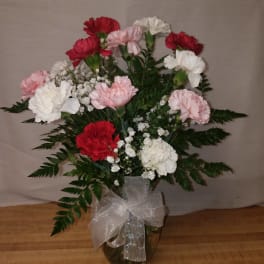 Bouquet of pink, red, and white carnations in a glass vase with a ribbon