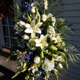 Tall white floral spray with lilies, roses, and blue accents