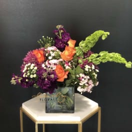 Orange roses and purple flowers in a square glass vase