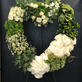 Heart-shaped floral wreath with white roses and green blooms on a stand
